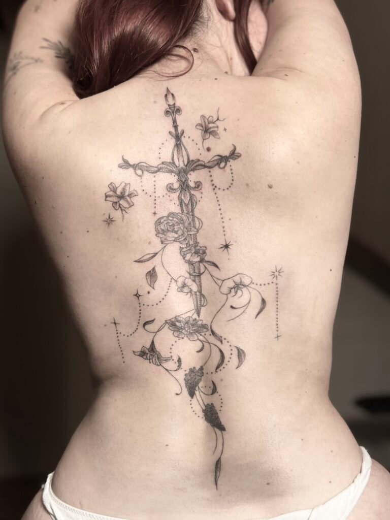 Grand tatouage ornemental dans le dos avec fleurs, épée et détails en dotwork