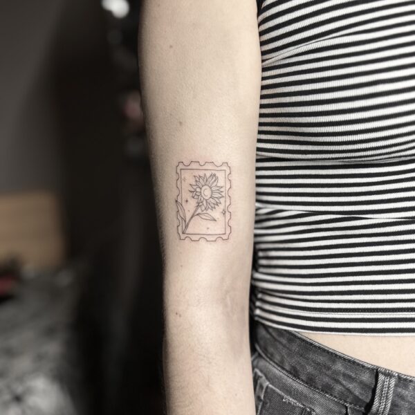 Petit tatouage fine line de timbre avec tournesol sur le bras